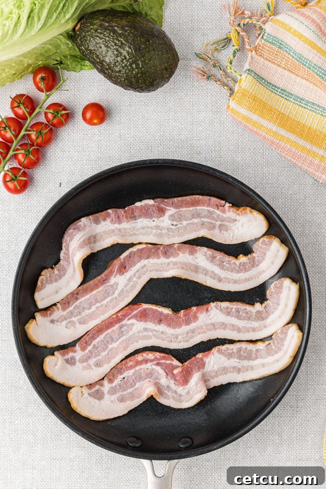 Frying strips of bacon in a hot pan, showing the initial cooking stage for the BLT salad.