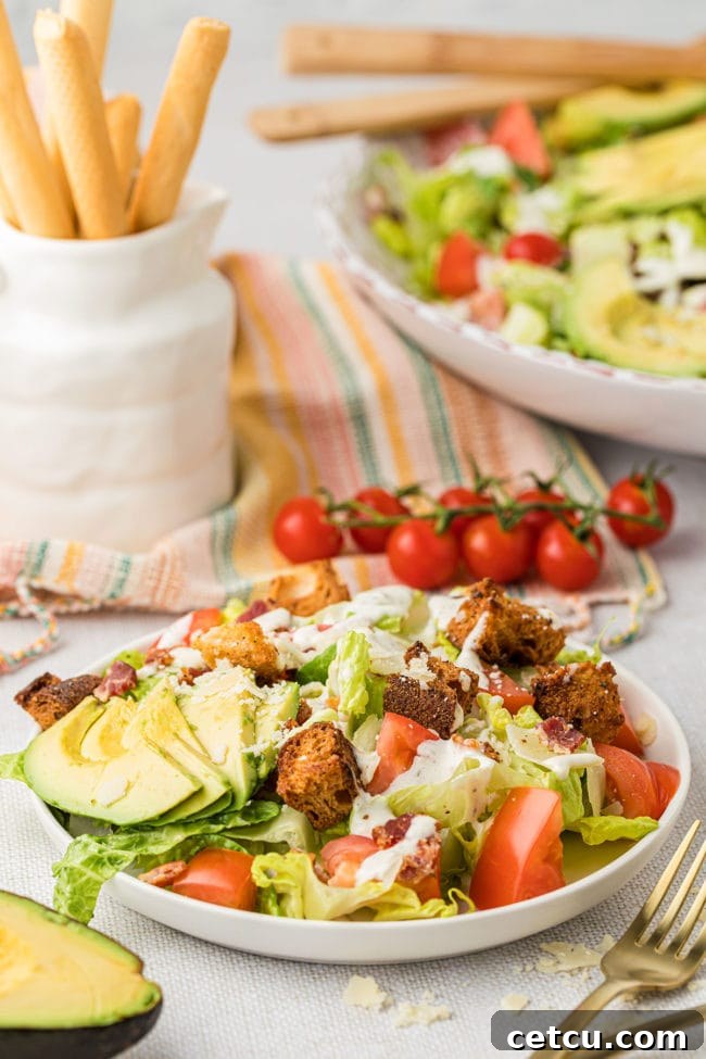 A close-up of a freshly prepared BLT salad with bacon, lettuce, tomato, and avocado, served on a white plate with dressing drizzled over.