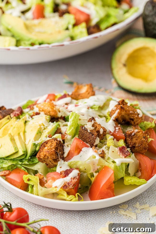 A bowl of freshly made BLT salad, garnished with vibrant green avocado slices, ready to be eaten.