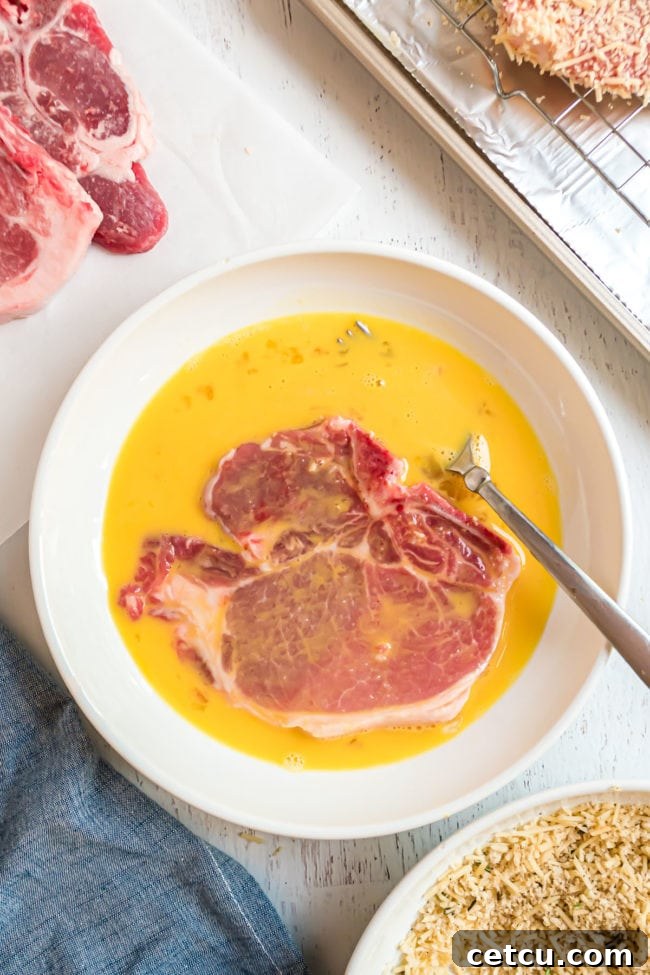 A raw pork chop being dipped into a bowl of lightly beaten eggs, preparing it for the panko coating.