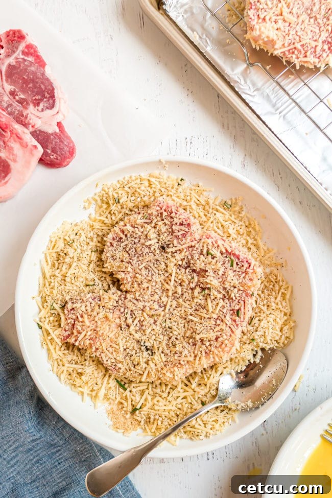 A pork chop being pressed into a bowl of the panko and Parmesan mixture, ensuring full and even coverage.