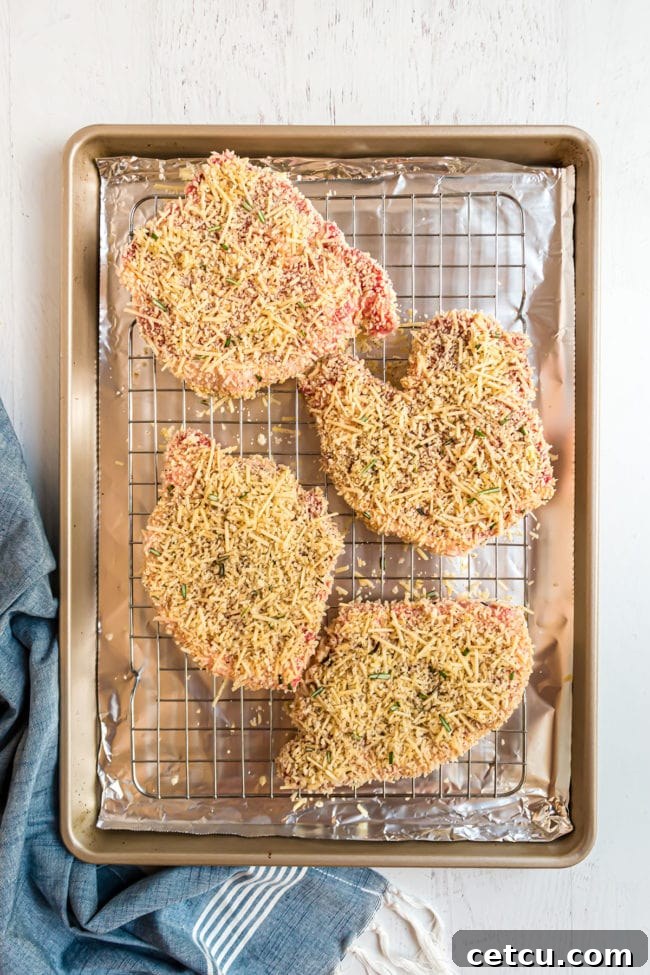 Coated Parmesan crusted pork chops arranged on a wire rack over a foil-lined baking sheet, ready for baking.