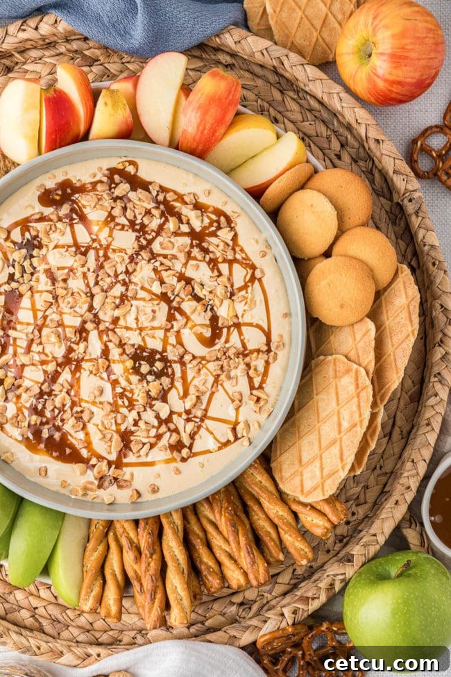 A vibrant dessert dip presented in a bowl, generously surrounded by an appealing assortment of fresh apples, crispy cookies, salty pretzels, and wholesome graham crackers, making for a perfect party spread.