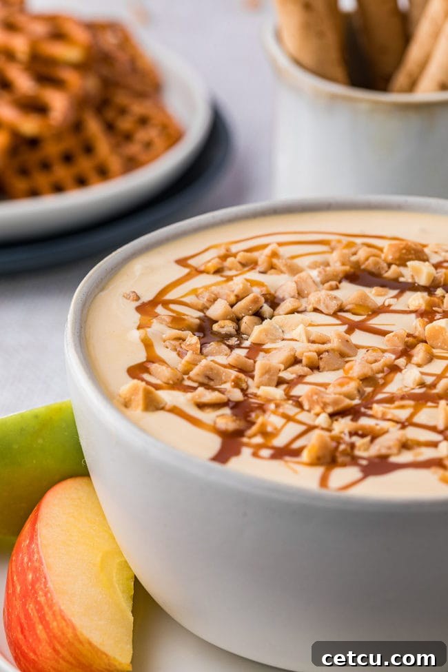 A close-up of creamy apple dip in a bowl, generously topped with a drizzle of luscious caramel and a scattering of finely chopped peanuts, ready for enjoyment.