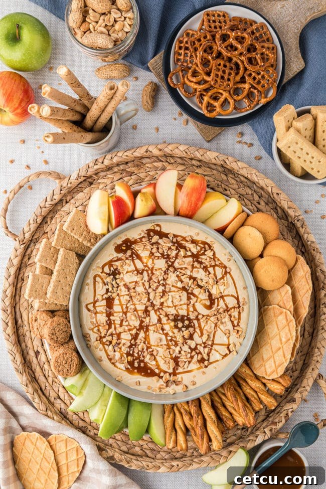 An enticing display of caramel apple dip served on a rustic tray, surrounded by an abundant assortment of crisp apple slices, crunchy cookies, and salty pretzels, creating a perfect snack or party centerpiece.