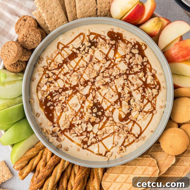 A beautiful bowl of caramel apple dip, artfully arranged with fresh apple slices, crunchy cookies, and graham crackers around it, inviting indulgence.