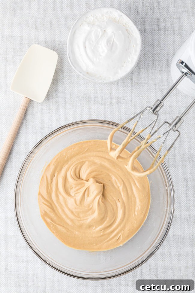 An electric mixer in action, smoothly blending the ingredients for apple dip in a transparent glass mixing bowl, creating a creamy base.