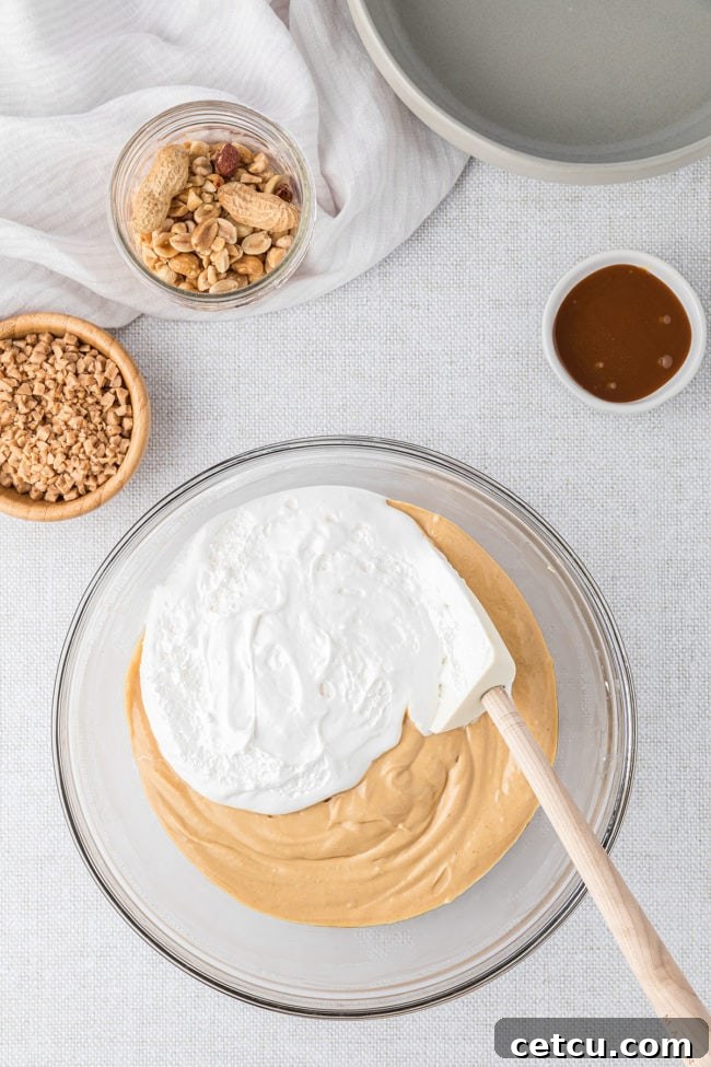 A delicate folding motion incorporating marshmallow crème into the already creamy caramel apple dip in a glass bowl, ensuring a light and airy texture.