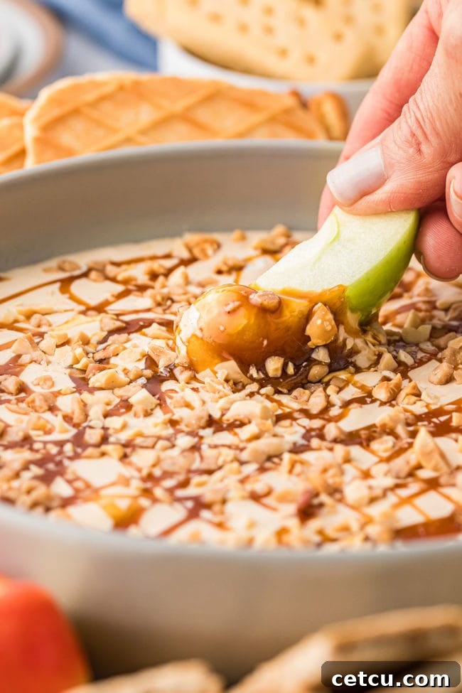 A woman elegantly dips a fresh, vibrant apple slice into a creamy dessert dip, showcasing the perfect pairing of fruit and treat.
