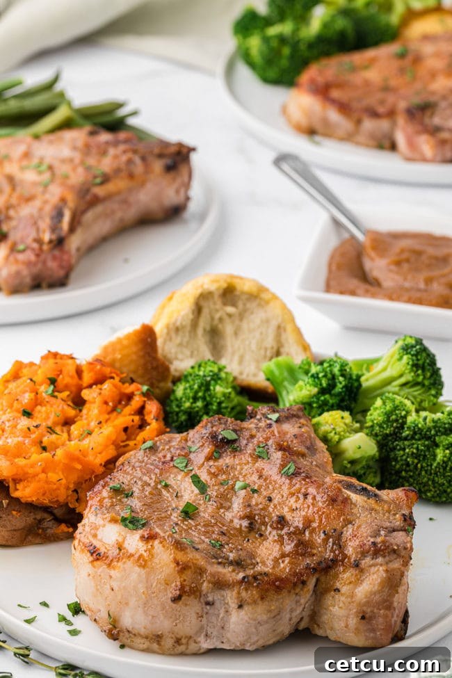 apple butter glazed pork chops on a plate with a baked sweet potato, broccoli and a dinner roll