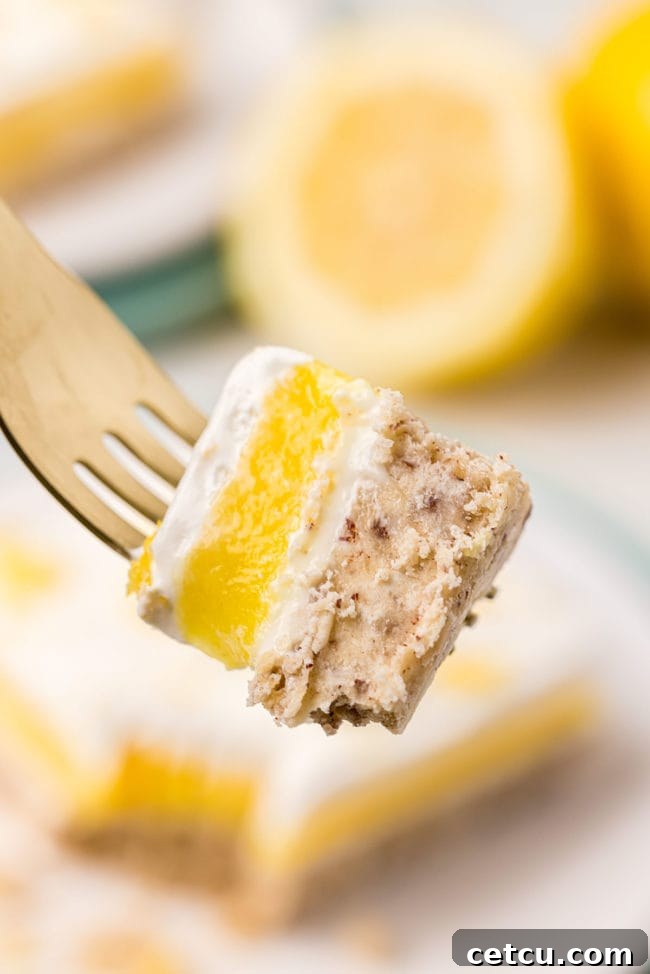 A close-up shot of a fork holding a perfect bite of Lemon Lush dessert, showcasing all the distinct creamy layers from crust to whipped topping. The bite appears refreshing and ready to be enjoyed.
