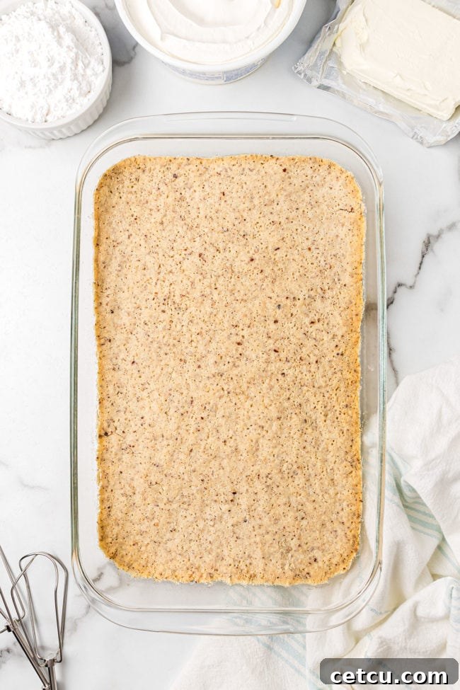 Close-up of a golden brown, crumbly pecan shortbread crust pressed into the bottom of a baking dish, freshly baked and ready for the next layer. The texture and evenness of the crust are clearly visible.