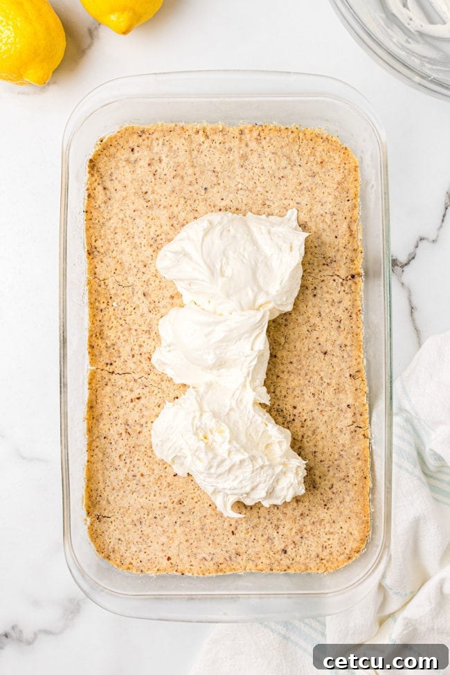 A thick, creamy layer of white cream cheese filling spread evenly over the cooled pecan shortbread crust in a baking dish, representing the second stage of preparing the lemon lush dessert.