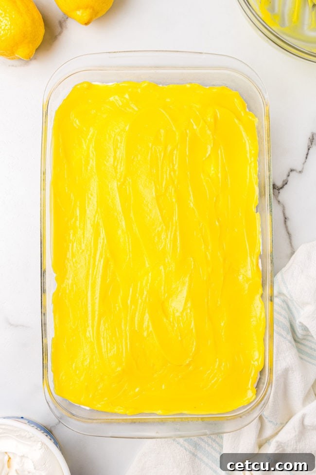 A vibrant, smooth layer of yellow lemon pudding spread meticulously over the cream cheese filling, clearly showcasing the third distinct layer of the Lemon Lush dessert in a baking dish.
