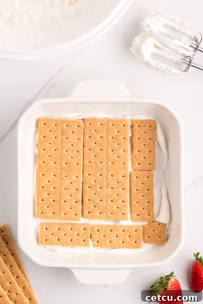 A layer of graham cracker sheets arranged neatly in a white baking dish, forming the base of the no-bake icebox cake.