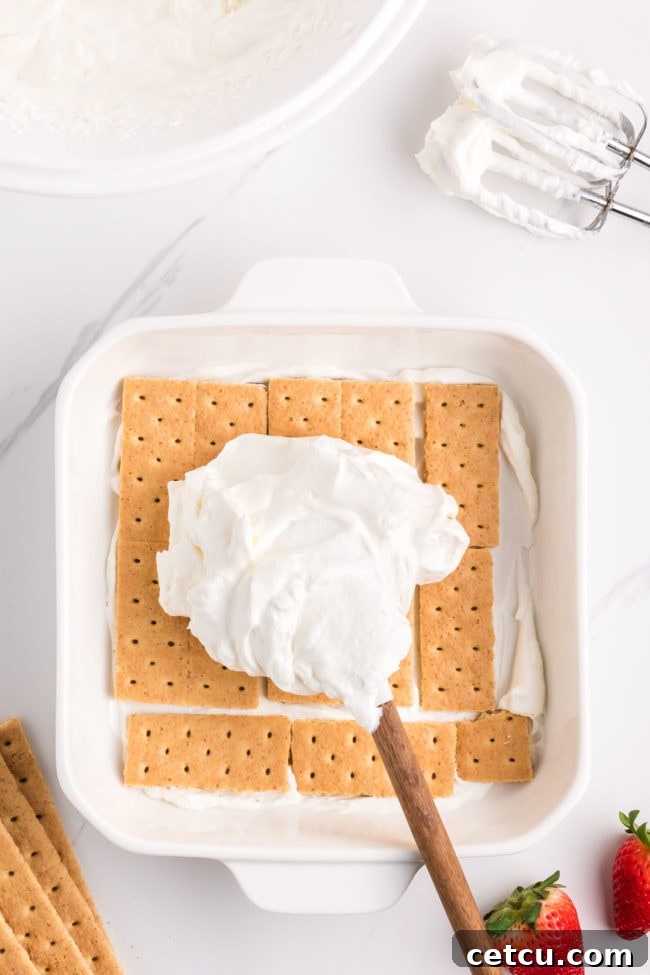 A smooth, even layer of freshly whipped cream being spread over graham crackers in an icebox cake, preparing for the next layer.