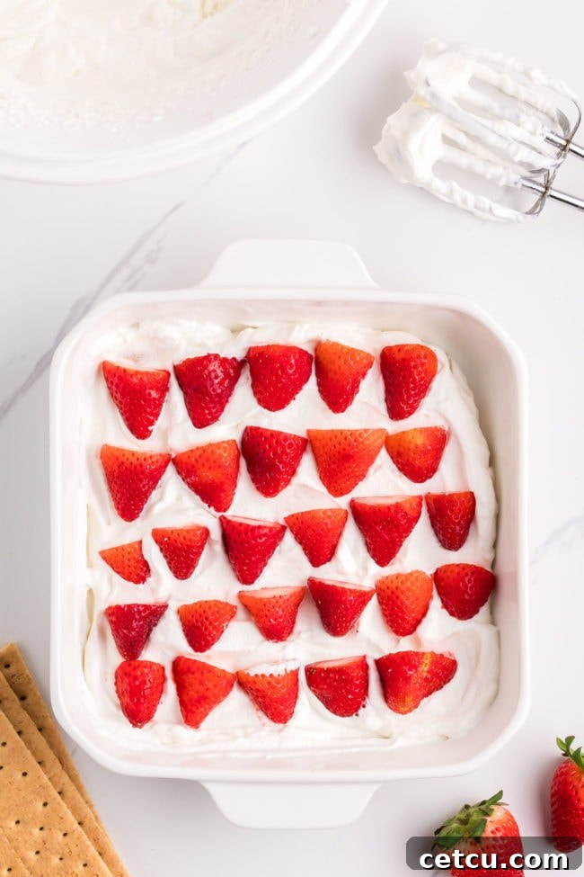 Bright red sliced strawberries carefully placed on a layer of whipped cream, adding vibrant color and fresh flavor to the icebox cake.