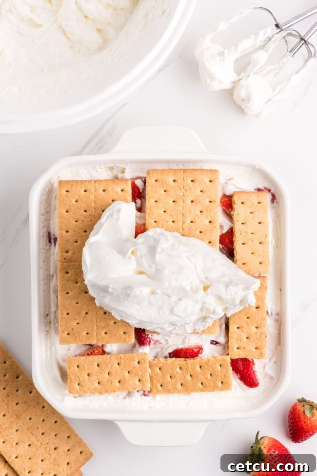 The final layer of whipped cream and strawberries completes the assembly of the no-bake strawberry icebox cake before chilling.