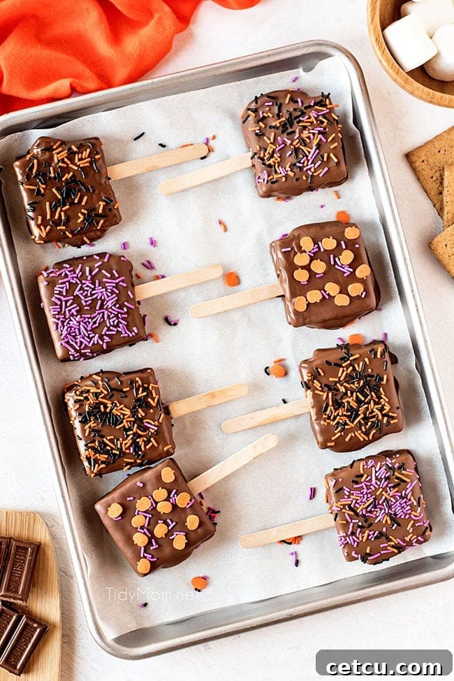Halloween S'mores Pops arranged on a baking pan lined with parchment paper, adorned with colorful sprinkles.