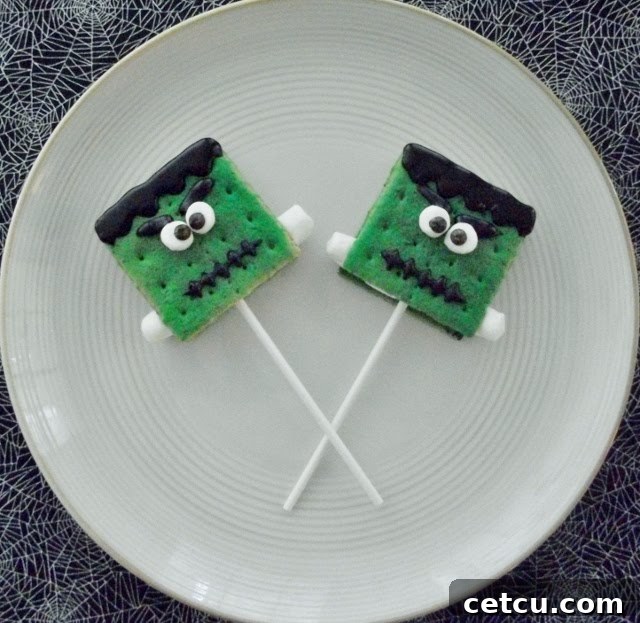 Close-up of Frankenstein themed S'mores Pops, green-dipped marshmallows with chocolate eyes and stitches, on sticks.