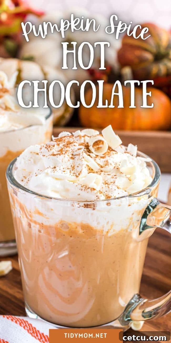 A festive image of pumpkin spice hot chocolate in a glass mug, with whipped cream, autumn leaves, and a cinnamon stick, evoking a cozy fall atmosphere.