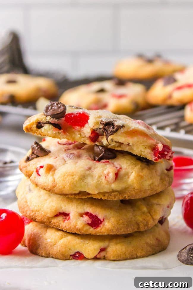 A charming stack of four chocolate chip cookies, each adorned with bright maraschino cherries, creating a festive look.