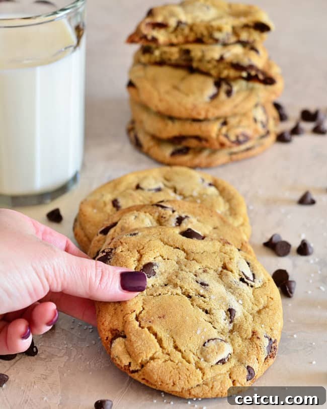 Two perfect chocolate chip cookies leaning against a tall glass of milk, inviting a classic pairing.