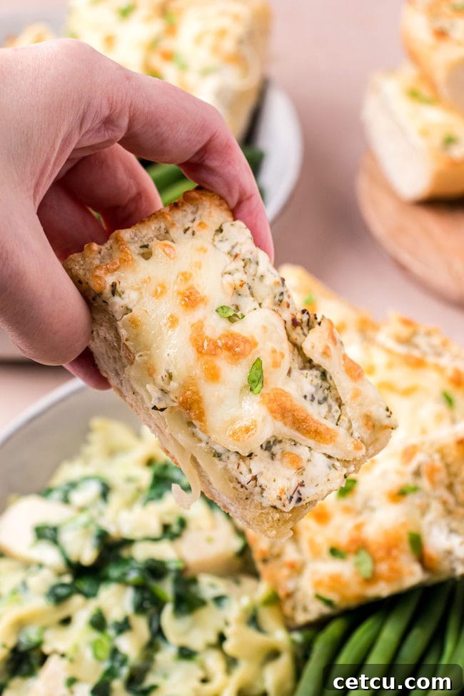 A hand holding a perfectly golden slice of Cheesy Garlic Bread, showing the gooey cheese and crisp crust.