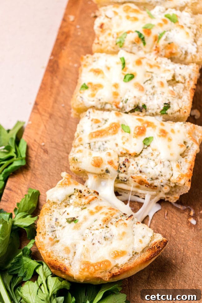 A large loaf of Cheesy Garlic Bread, sliced and pulled apart, showing the melted cheese and soft interior.