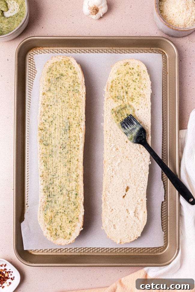 A French bread loaf sliced lengthwise, with the seasoned garlic butter being brushed evenly over the cut surface.