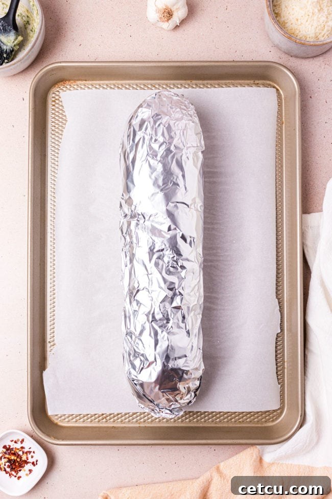 The buttered halves of French bread reunited and wrapped in aluminum foil, ready for initial baking.