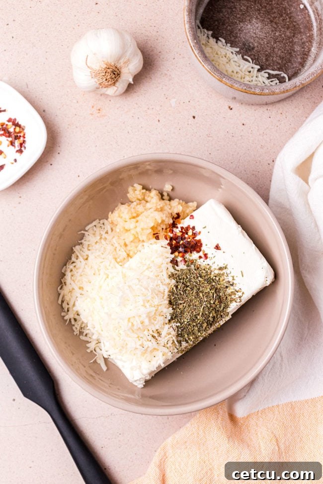 Softened cream cheese, grated Parmesan, minced garlic, Italian seasoning, and red pepper flakes in a bowl, before mixing.
