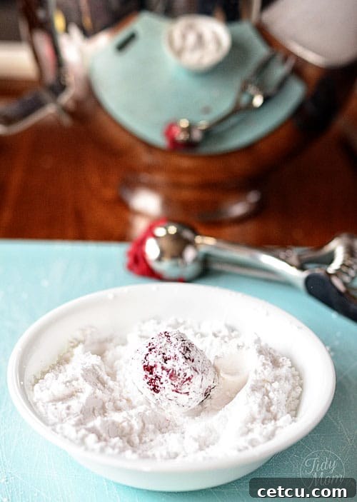 Hands rolling a red velvet cookie dough ball in powdered sugar