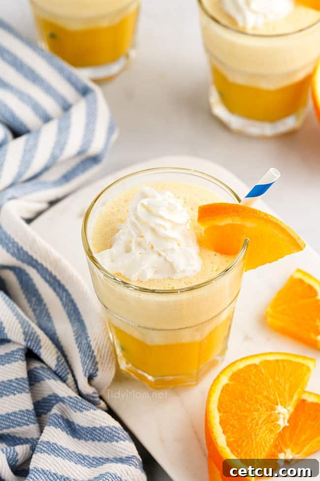 A glass of homemade Orange Julius, beautifully garnished with fresh orange slices, sits on a surface, looking refreshing and inviting.