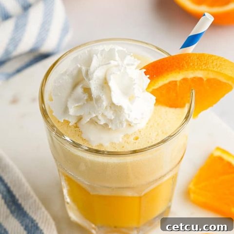 A glass filled with a frothy Orange Julius, perfectly topped with whipped cream and a blue straw, showcasing the final, irresistible blended drink.