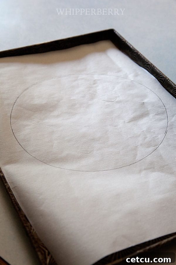 A hand spreading meringue onto a parchment-lined baking sheet, guided by a drawn circle.