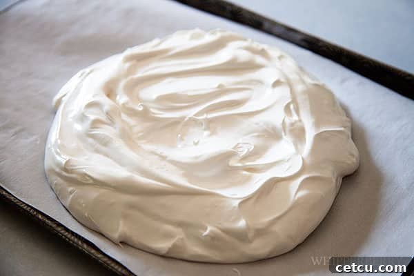 Close-up of meringue spread into a circle on a baking sheet, forming a nest-like base.