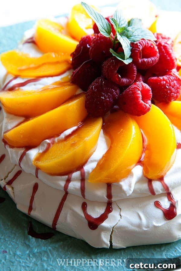 A fully assembled Peach Melba Pavlova, featuring a meringue base topped with whipped cream, fresh peaches, and raspberries, on a decorative tray.