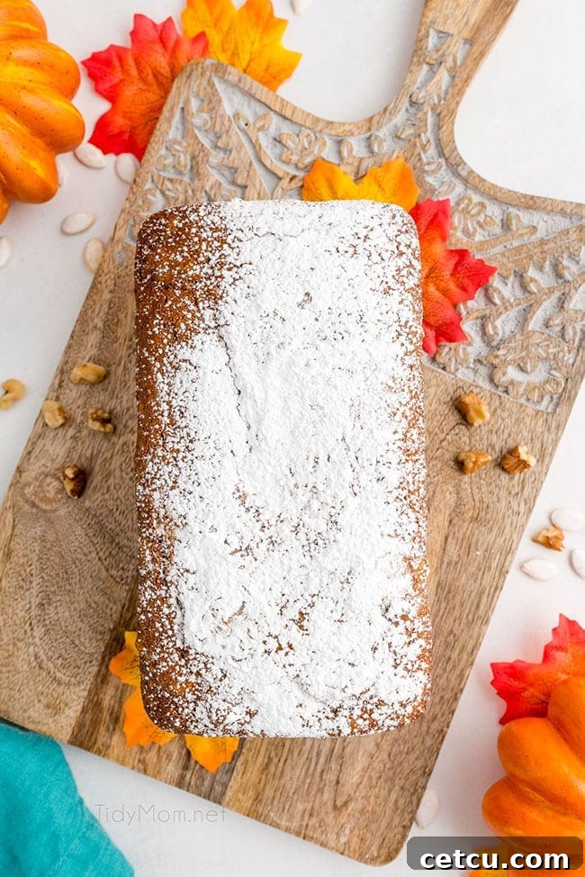 A freshly baked loaf of pumpkin bread, delicately dusted with powdered sugar, sits on a rustic surface, inviting a taste of autumn.