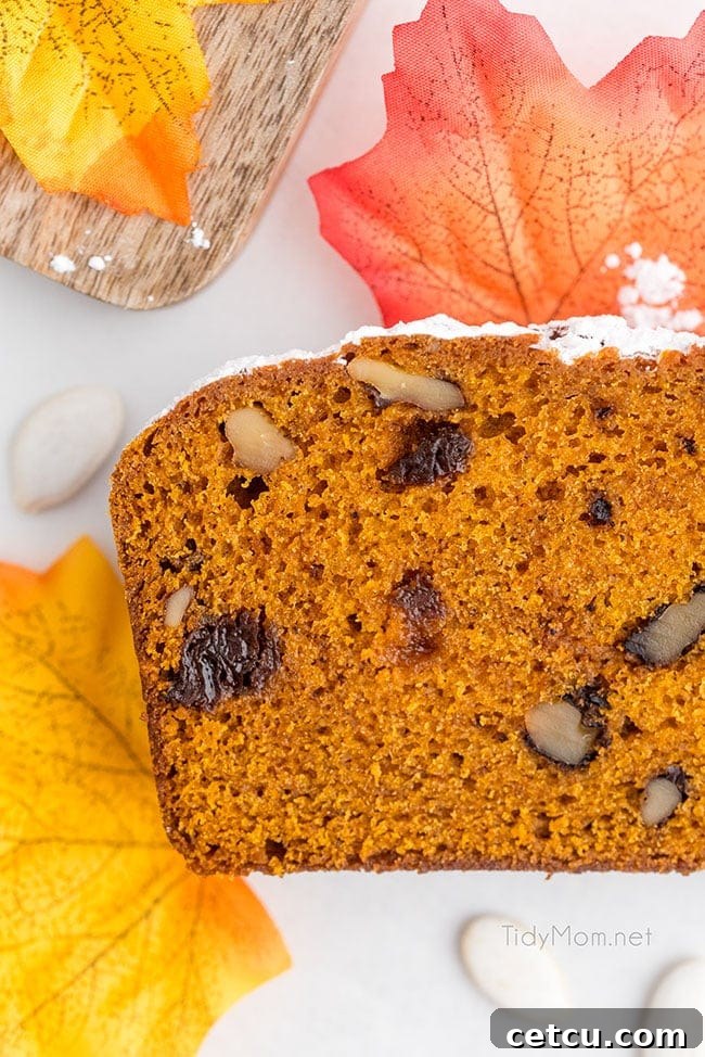 A warm slice of pumpkin bread, adorned with a scattering of festive fall leaves, rests elegantly on a wooden counter, capturing the essence of autumn.