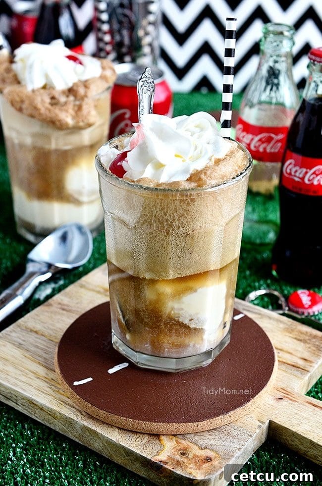 Two tall glasses filled with Classic Coke Floats, topped with whipped cream and a maraschino cherry, ready to be enjoyed.