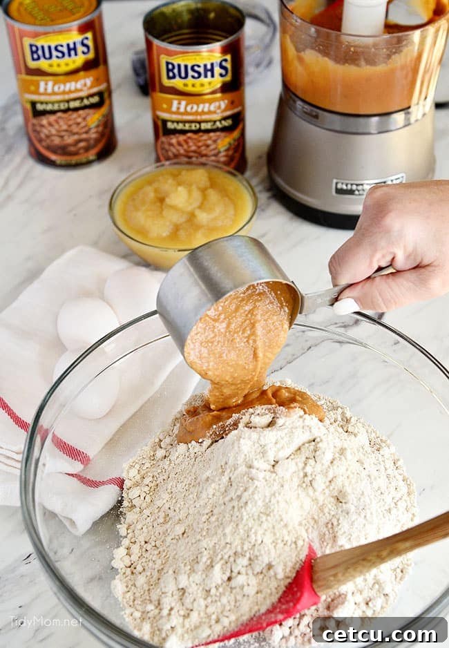A mixing bowl filled with muffin batter, showing pureed baked beans being poured in, illustrating the secret ingredient addition.