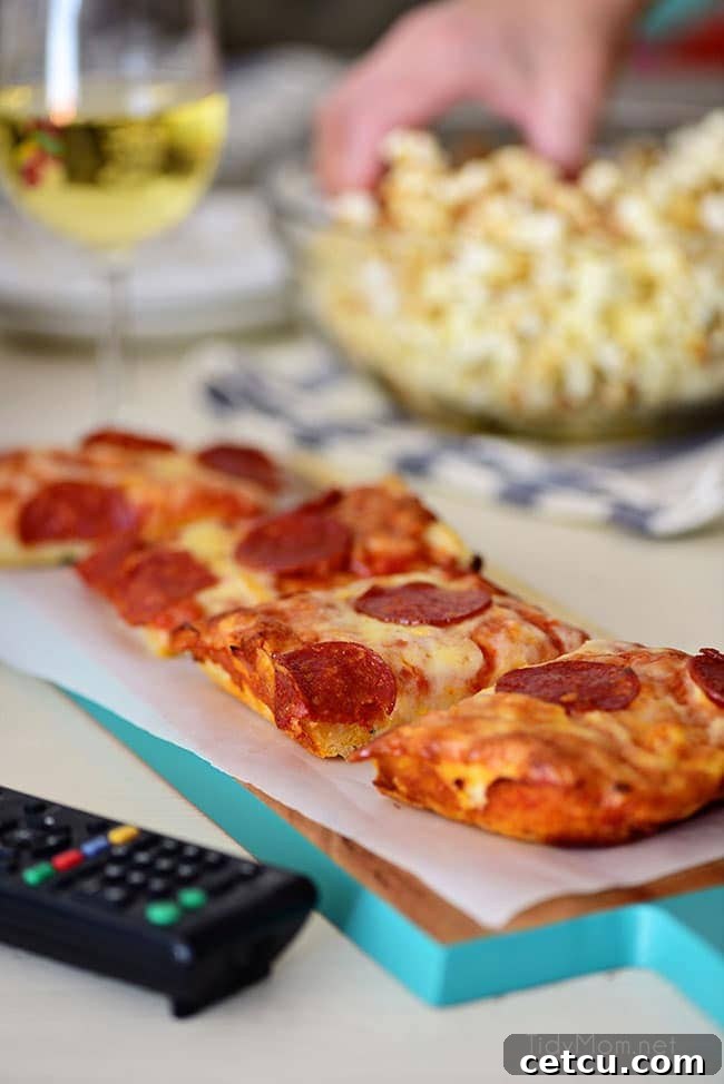Creating a special movie night at home with DIGIORNO pizza and homemade Sweet Heat Maple-Chili Popcorn. This vertical shot captures the deliciousness of an oven-fresh pizza and a bowl of gourmet popcorn, ideal for a cozy date or family entertainment. Get the recipe for the unique popcorn on TidyMom.net