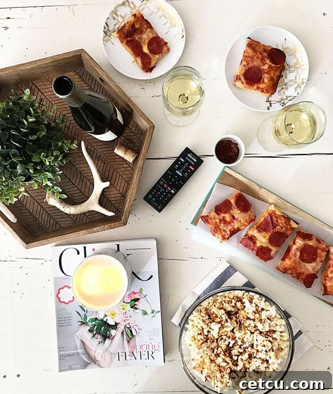 Overhead flat lay shot of a cozy movie night spread, featuring Sweet Heat Maple-Chili Gourmet Popcorn, DIGIORNO pizza slices, and refreshing drinks. This inviting scene captures the essence of a perfect at-home date or family movie night. Get the popcorn recipe at TidyMom.net.