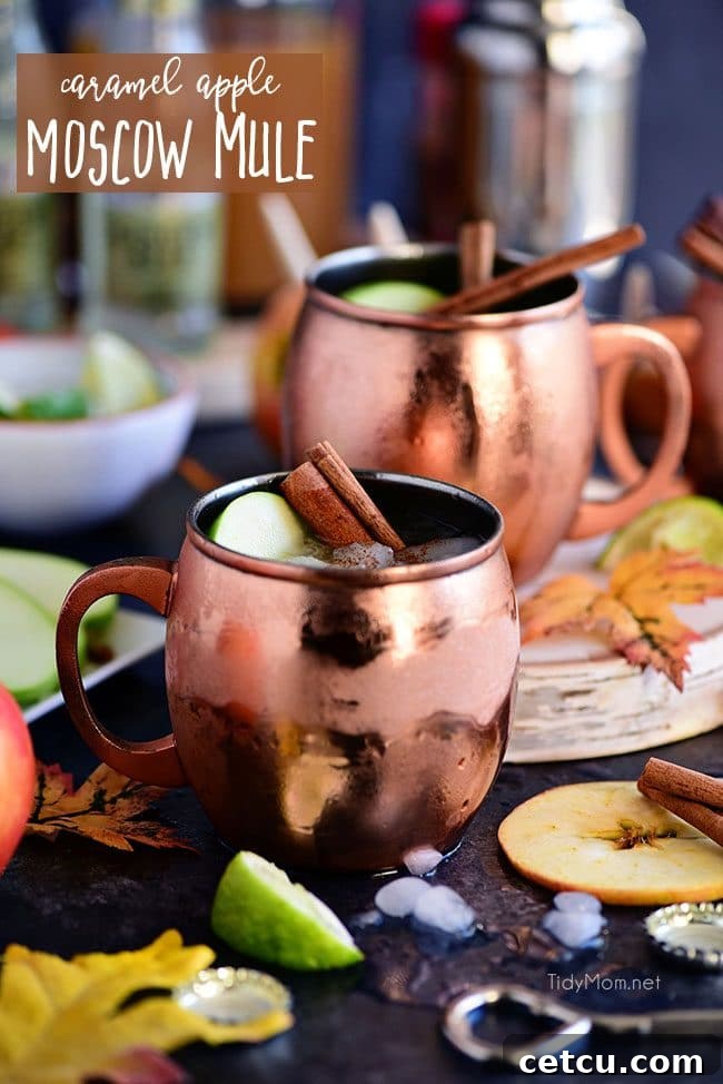 A Caramel Apple Moscow Mule in a copper mug, garnished with apple slices, a cinnamon stick, and a sprig of rosemary, perfect for autumn festivities.