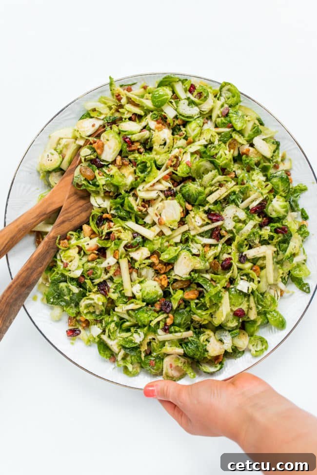 A vibrant Waldorf Brussels Sprout Salad, featuring shaved Brussels sprouts, apples, cranberries, and bacon, in a large serving bowl.