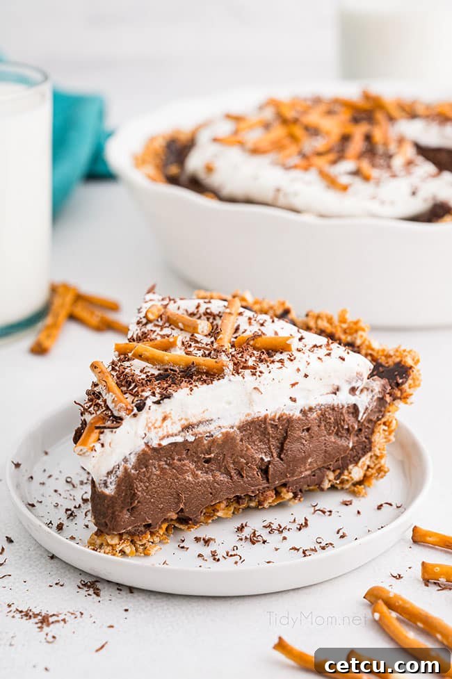 A slice of rich Chocolate Pudding Pie with a pretzel crust on a white plate, showcasing its layers of chocolate, whipped cream, and pretzel base.