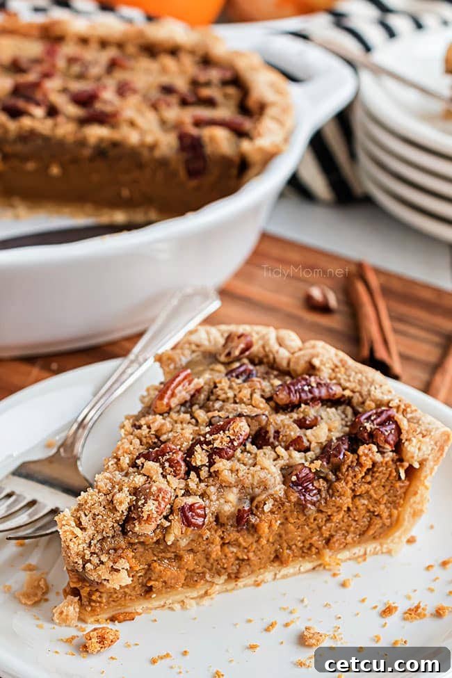 A slice of Apple Butter Pumpkin Pie with Streusel Topping on a white plate with a fork, showing its rich filling and crumbly top.