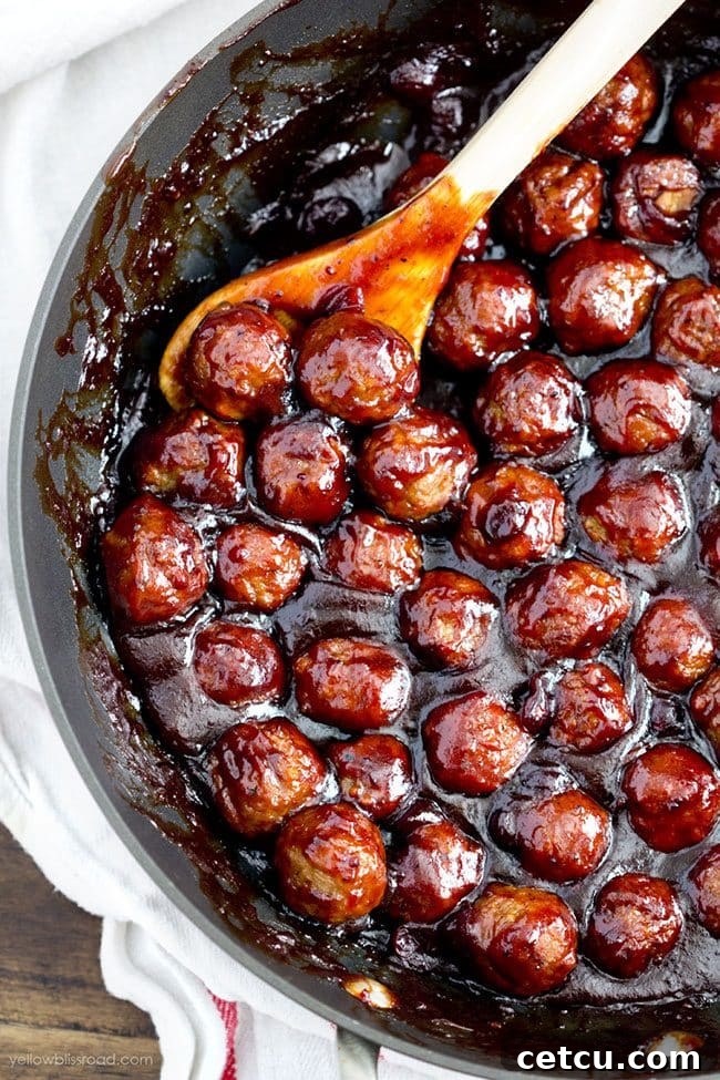 A dish of Spicy Cranberry Meatballs from Yellow Bliss Road, glistening with sauce and garnished, ready to be served as an appetizer.