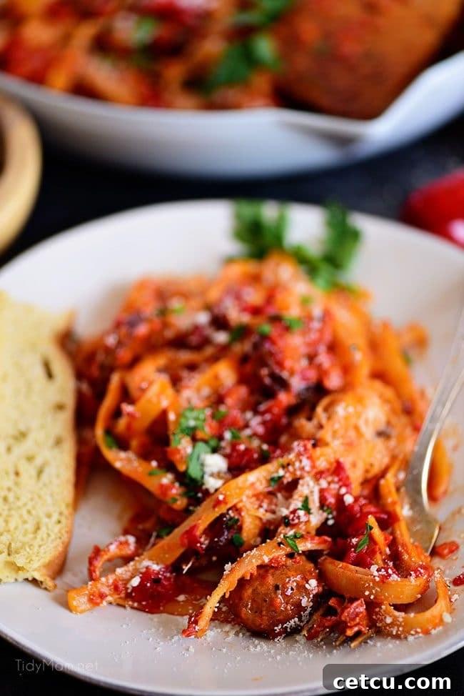 Close-up of creamy Roasted Red Pepper Fettuccine with succulent smoked sausage on a white plate, garnished with fresh herbs.